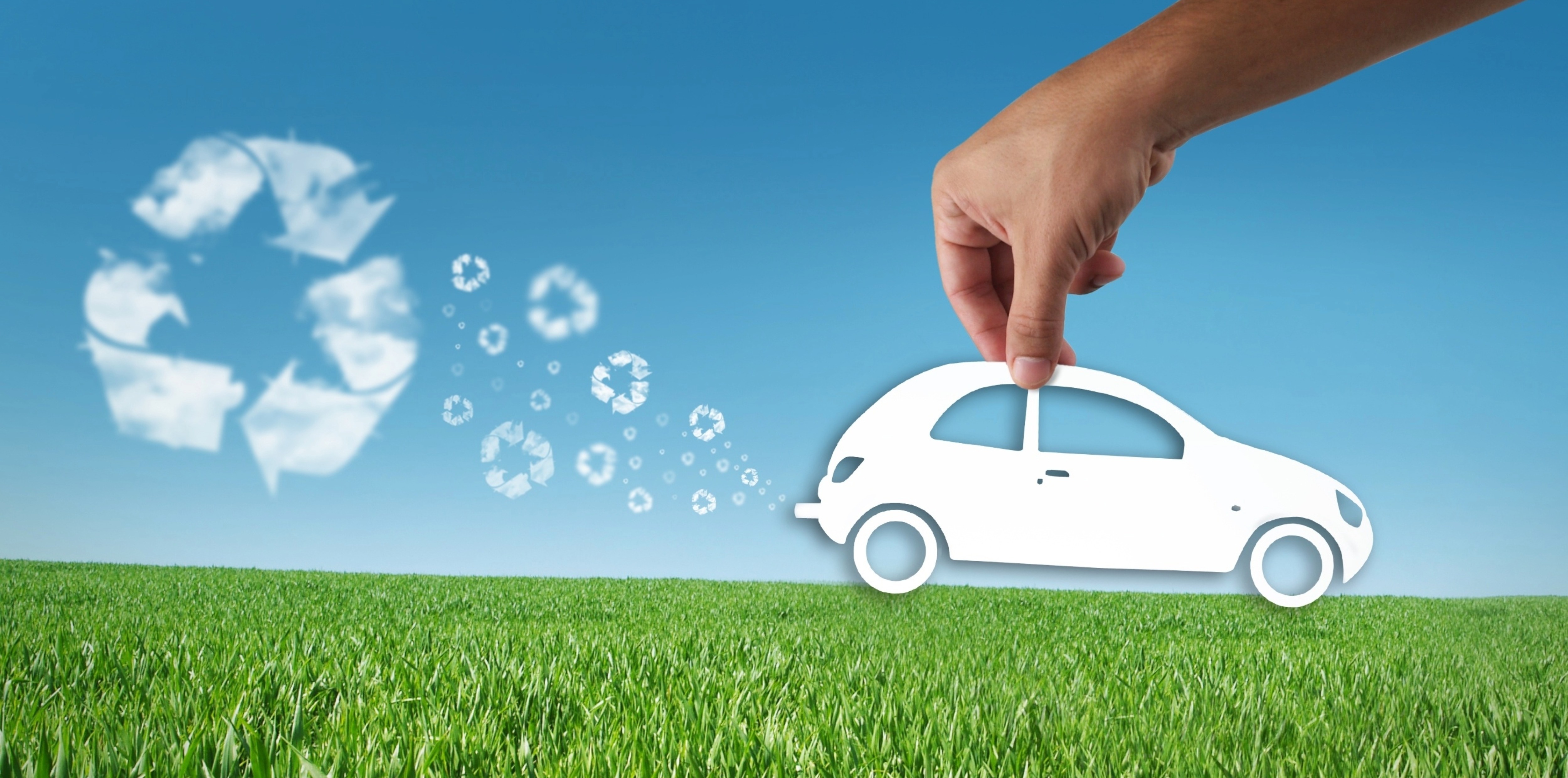Symbolbild Kreislaufwirtschaft im Automobilbau: Papierschnitt eines Autos vor grüner Wiese, im Hintergrund Recycling-Symbole als Wolkenform